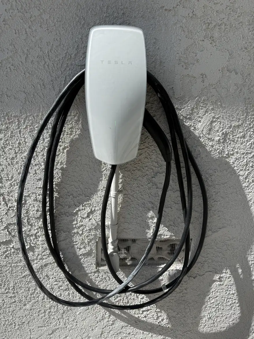 Tesla Wall Connector installed on a stucco wall with the charging cable wrapped
