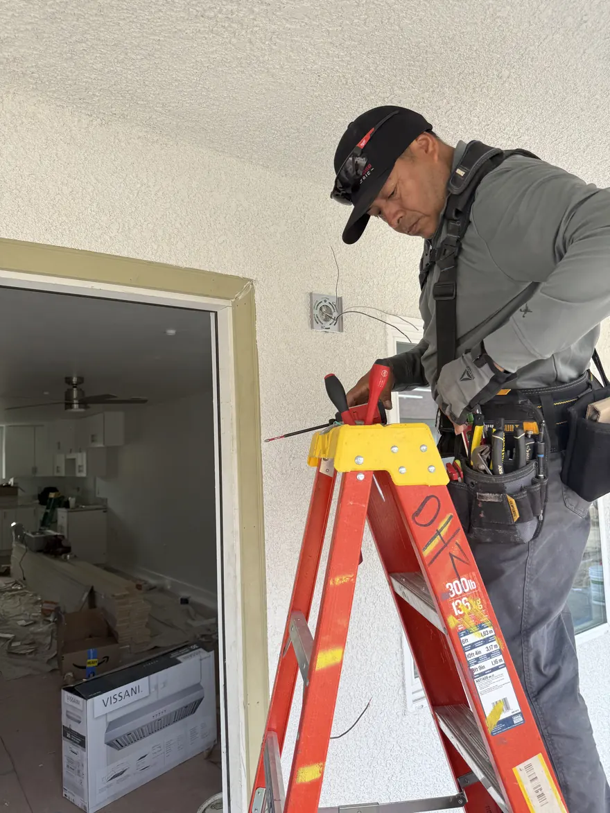 ElitePhase electrician working from a ladder, wiring a ceiling box during a remodel